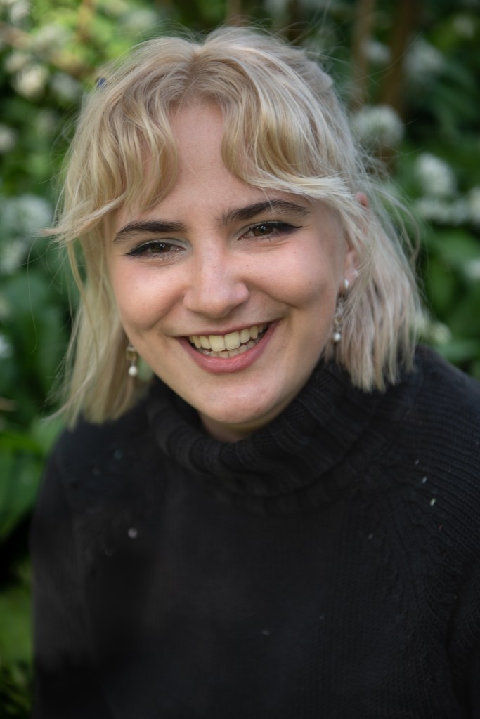 Portrait of a blonde woman laughing against a blurred white flower background