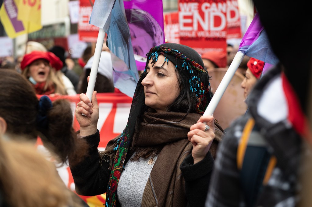 A woman with beaded headscarf holding a flag during the Million Women Rise protest, London