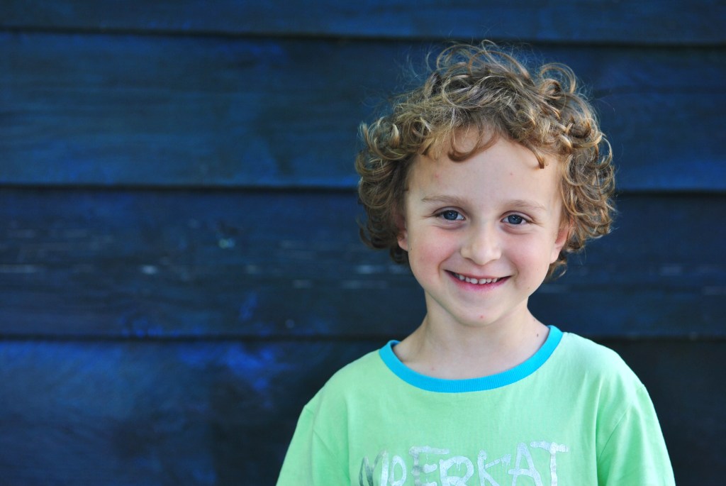 Portrait of a young boy with curly hair smiling agaist a blue boarded background