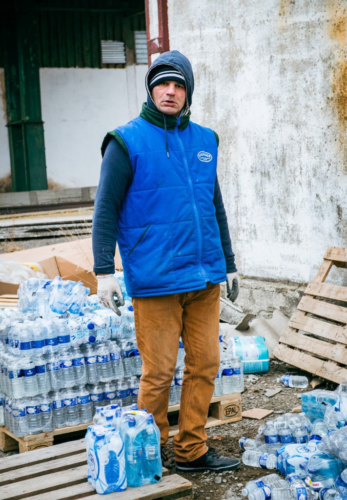 A volunteer for a Romanian NGO providing aid to Ukraine looking at the camera, with bottled water around him