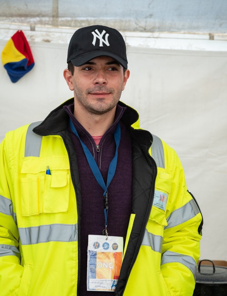 A volunteer in a tent at the Siret border in Romania, wearing a fluorescent jacket and volunteer lanyard.  